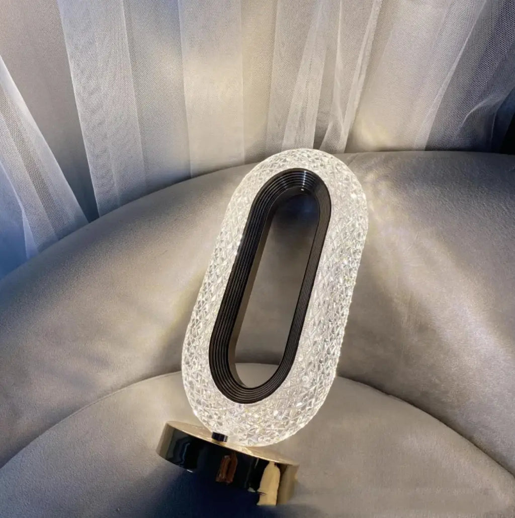 A sleek oval-shaped crystal touch desk lamp with a sparkling crystal exterior and black inner ring for luxury decor
