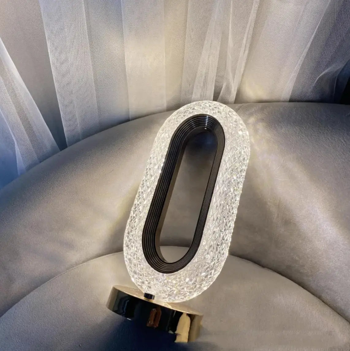 A sleek oval-shaped crystal touch desk lamp with a sparkling crystal exterior and black inner ring for luxury decor