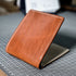 A tan leather short wallet with white stitching resting on a grid-patterned surface for men’s fashion use