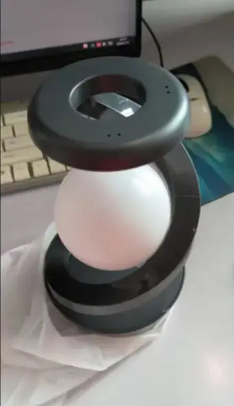 Black magnetic rotating moon desk lamp with white spherical bulb and wireless charger suspended in center