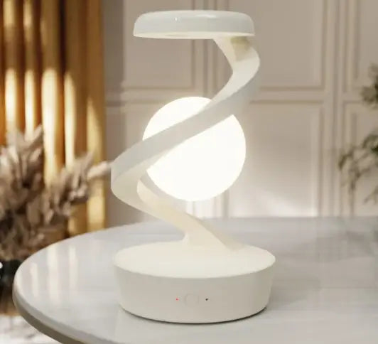 A sleek white rotating moon desk lamp with a glowing spherical bulb and wireless charger in minimalist design